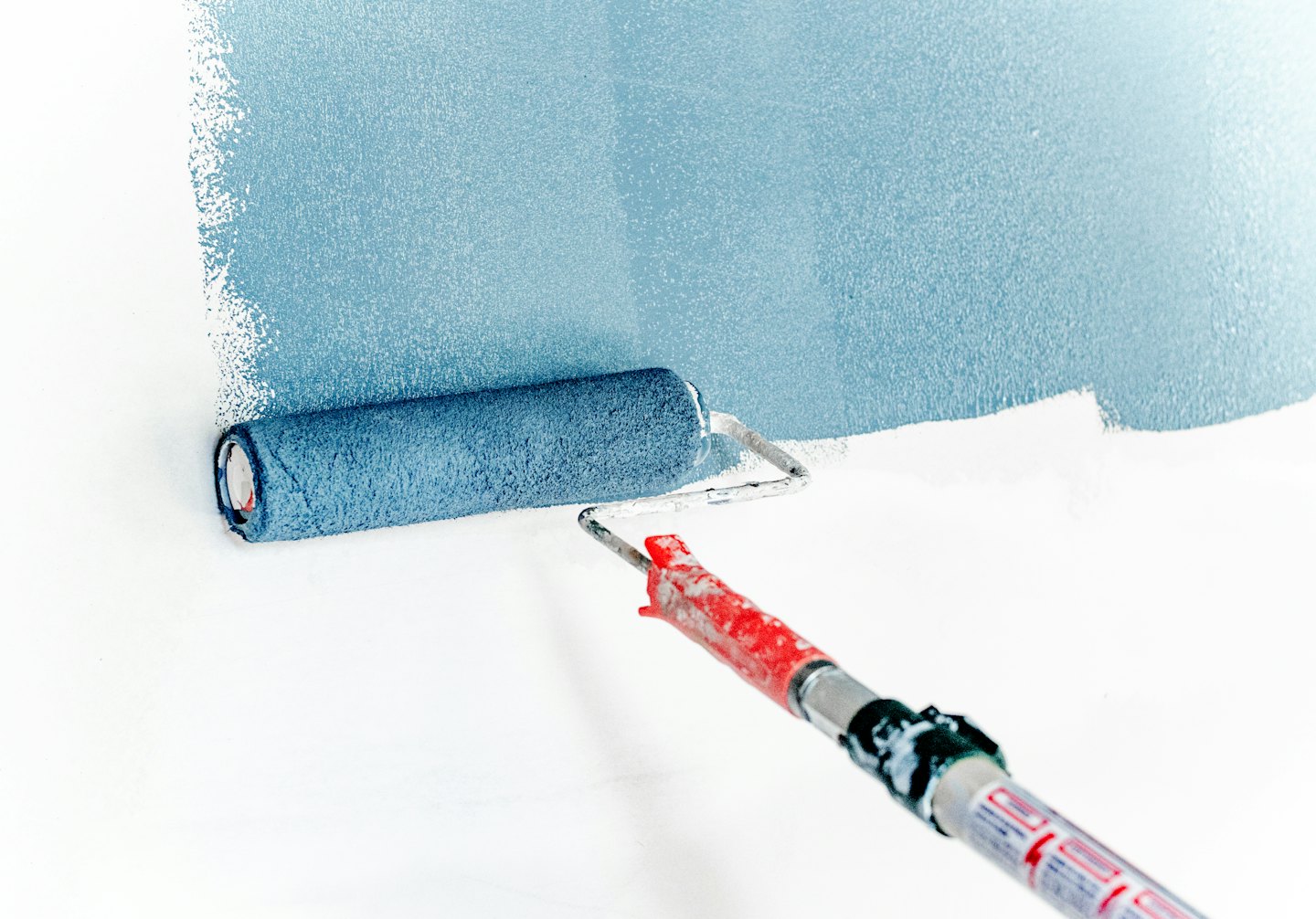 Rodillo de pintura aplicando pintura azul claro a una pared blanca.