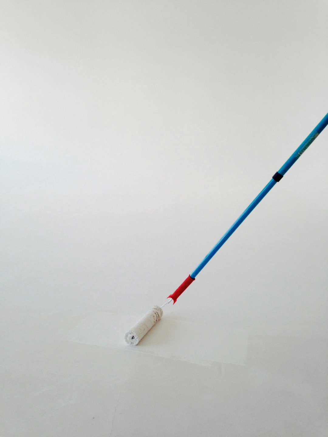 Pintando una pared con un rodillo de mango azul y rojo.